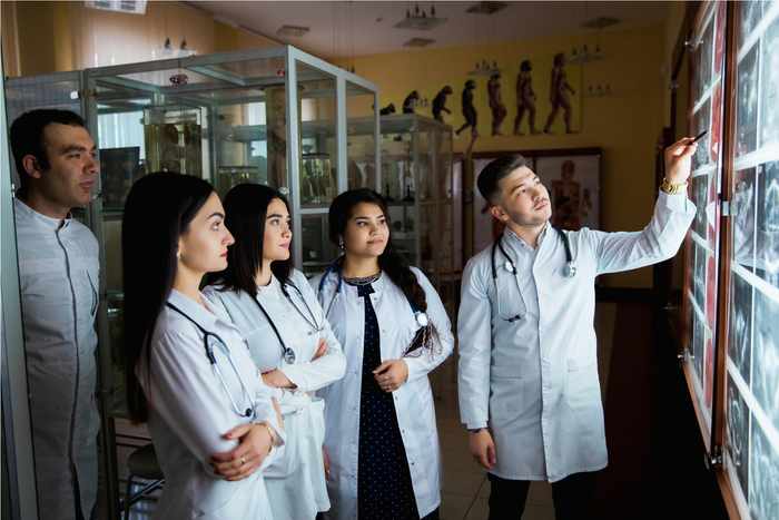 Fotografía de un médico egresado de la maestría en educación médica en una oficina de un hospital revisando radiografías con un tres doctoras y un doctor.