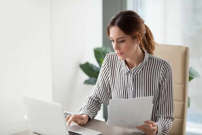 Fotografía de una mujer egresada de la especialidad en finanzas, revisando un análisis financiero en su computadora y hojas impresas.